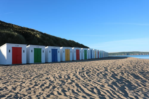 multi-coloured beach huts along woolacombe beach on blue sunny day