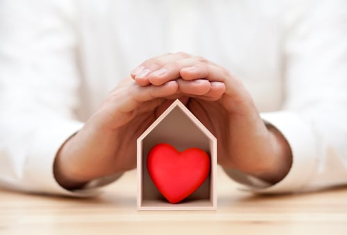 wooden house with red heart protected by hands
