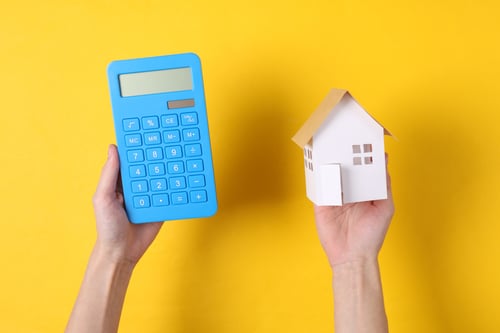 hands hold a calculator and model house on yellow background