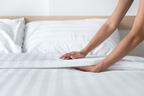 hands set up white bed sheets in bedroom